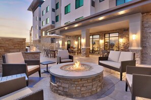 Un espace extérieur aménagé en terrasse, avec des meubles en osier, un foyer en pierre et une vue sur l’intérieur du bâtiment.