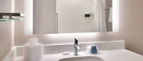 Un baño moderno con un espejo grande, un lavamanos blanco y un estante de vidrio.