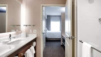 A modern hotel bathroom with a large mirror, two sinks, and a shower area.