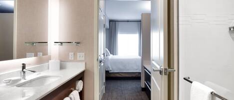 A modern hotel bathroom with a large mirror, two sinks, and a shower area.