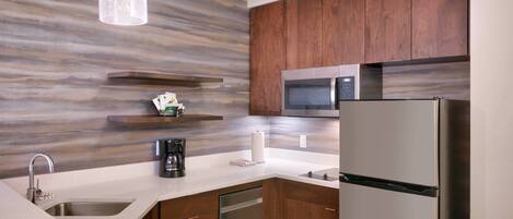 A modern kitchen with a stainless steel refrigerator, a microwave, and a dishwasher. There are wooden cabinets and a marble countertop.