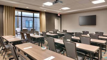 A conference room with multiple tables and chairs, a projector, and a large screen on the wall.