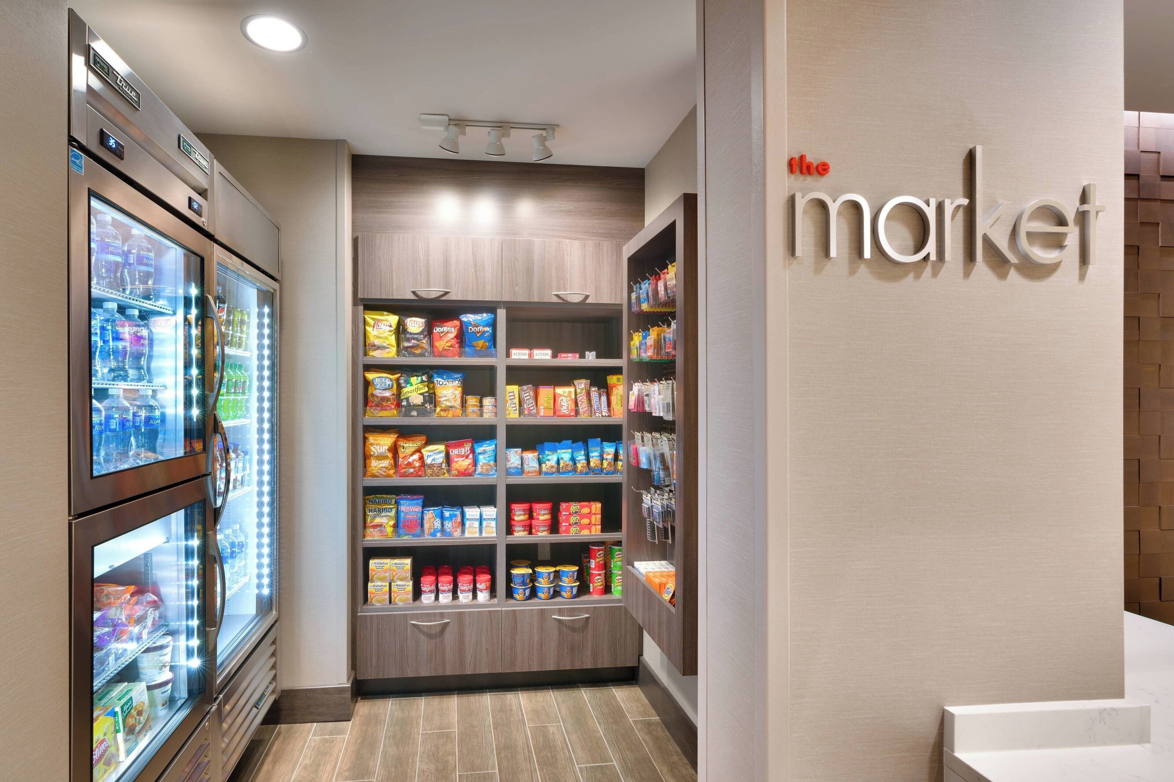 A grocery store interior with refrigerated sections, shelves stocked with snacks, and a sign reading "the market".