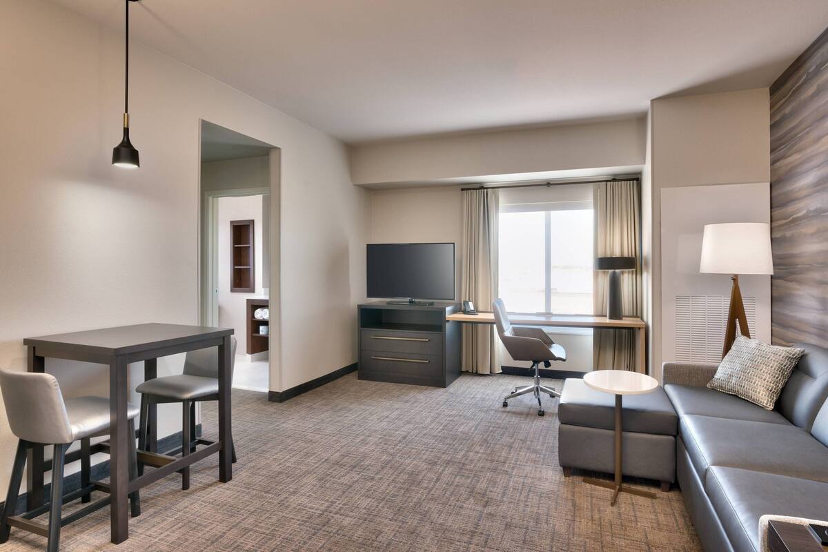 A hotel room with a desk, two chairs, a sofa, a TV, and a lamp.