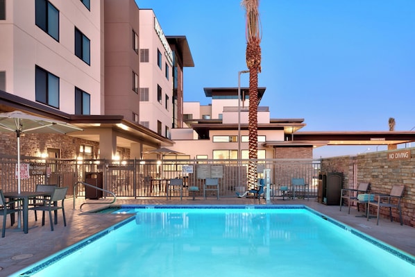 Una piscina al aire libre con un edificio moderno de fondo, una palmera y un área de estar exterior.