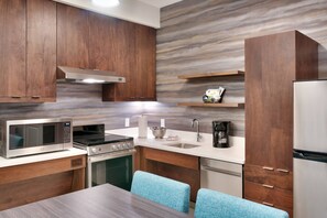 A modern kitchen with wooden cabinets, a stainless steel microwave, stove, and refrigerator, and a dining area with blue chairs. - Residence Inn by Marriott Phoenix West/Avondale (Avondale)