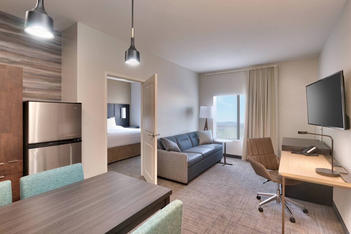 A hotel room with a bed, a desk, a chair, a sofa, a TV, and a dining area.