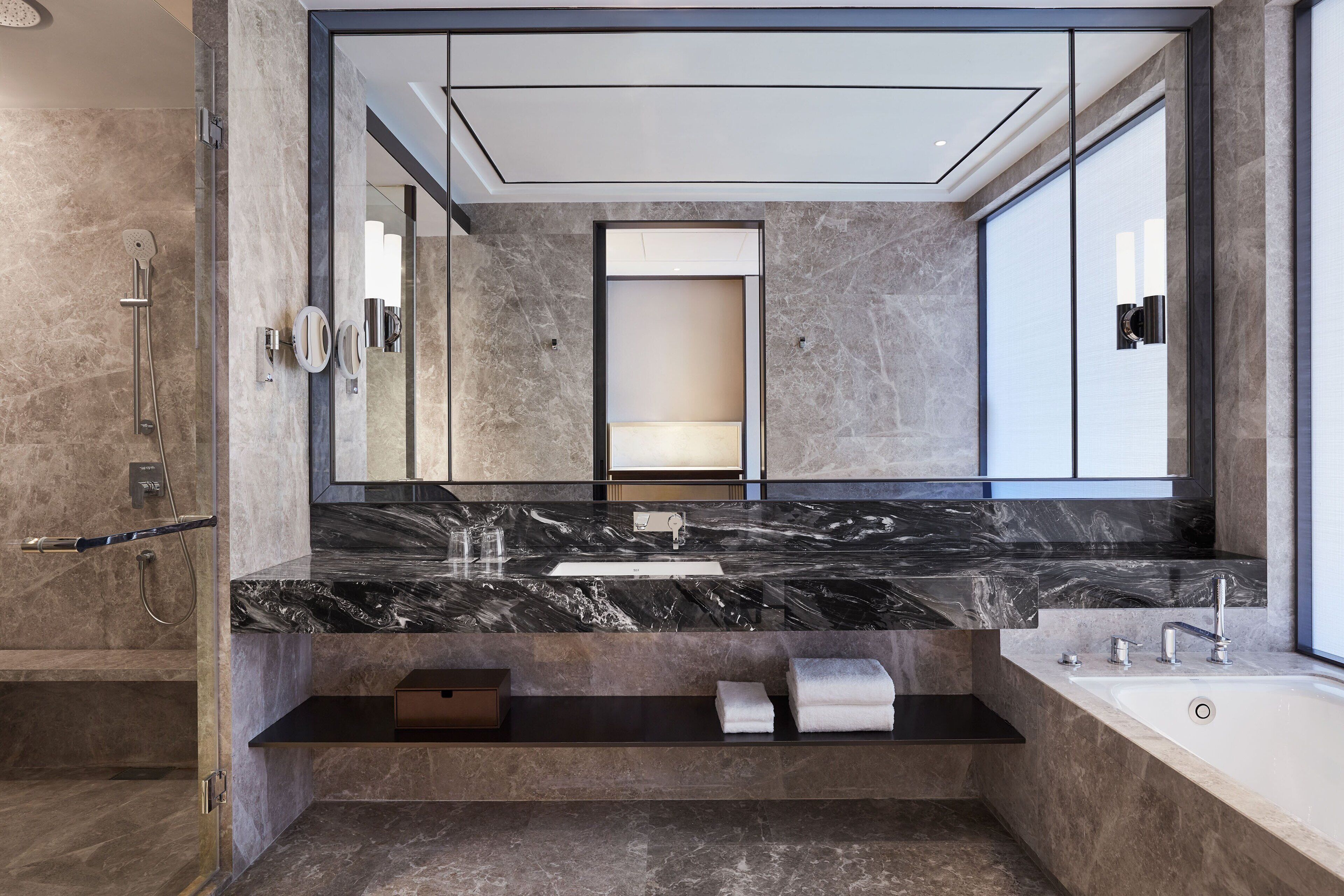 A modern bathroom with a large mirror, marble countertop, built-in shower, and a bathtub.