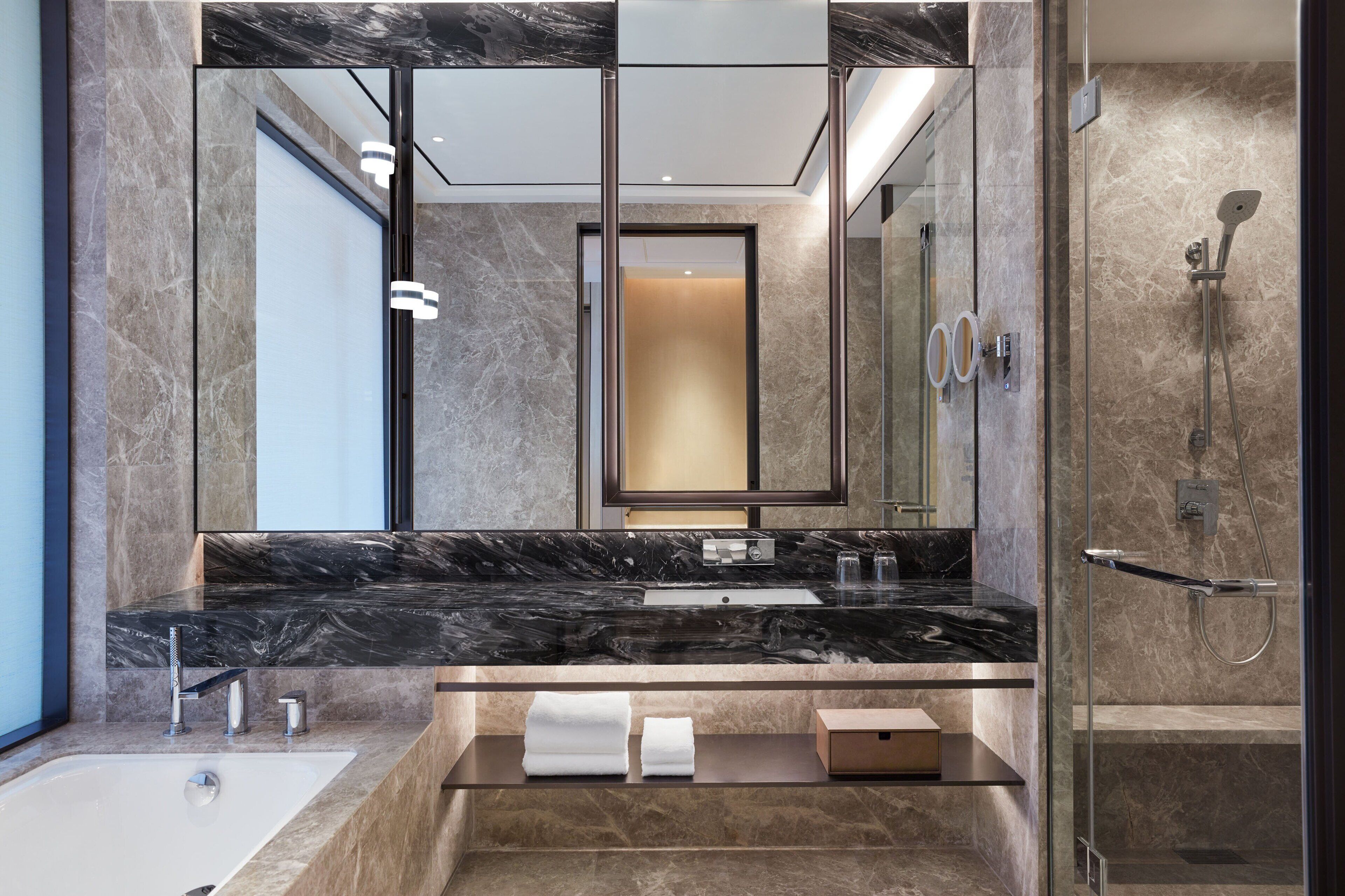 A modern bathroom with a marble sink, a large mirror, a glass-enclosed shower, and a built-in towel warmer.