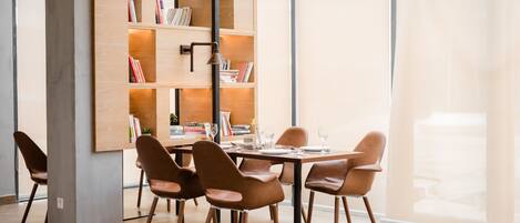 A modern dining area with a wooden bookshelf, leather chairs, and a glass table set for dining.