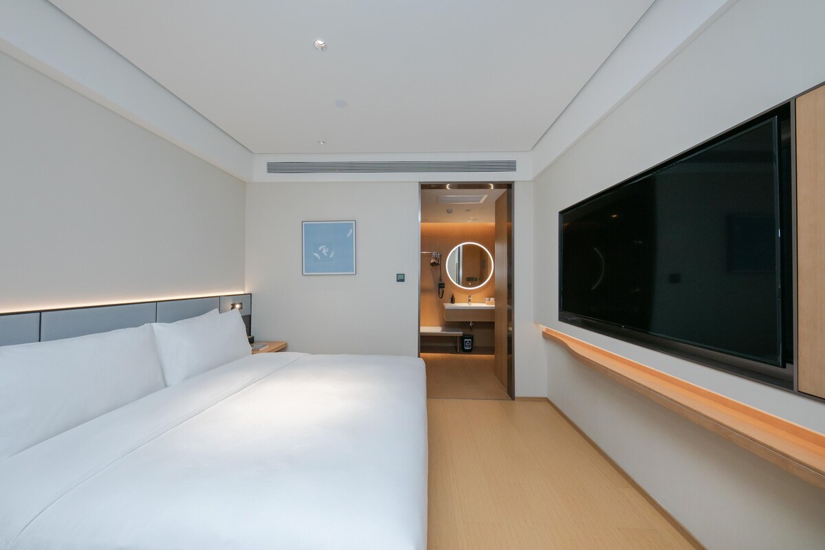 Habitación de hotel moderna con una cama grande, un televisor y un baño visible a través de una puerta abierta.