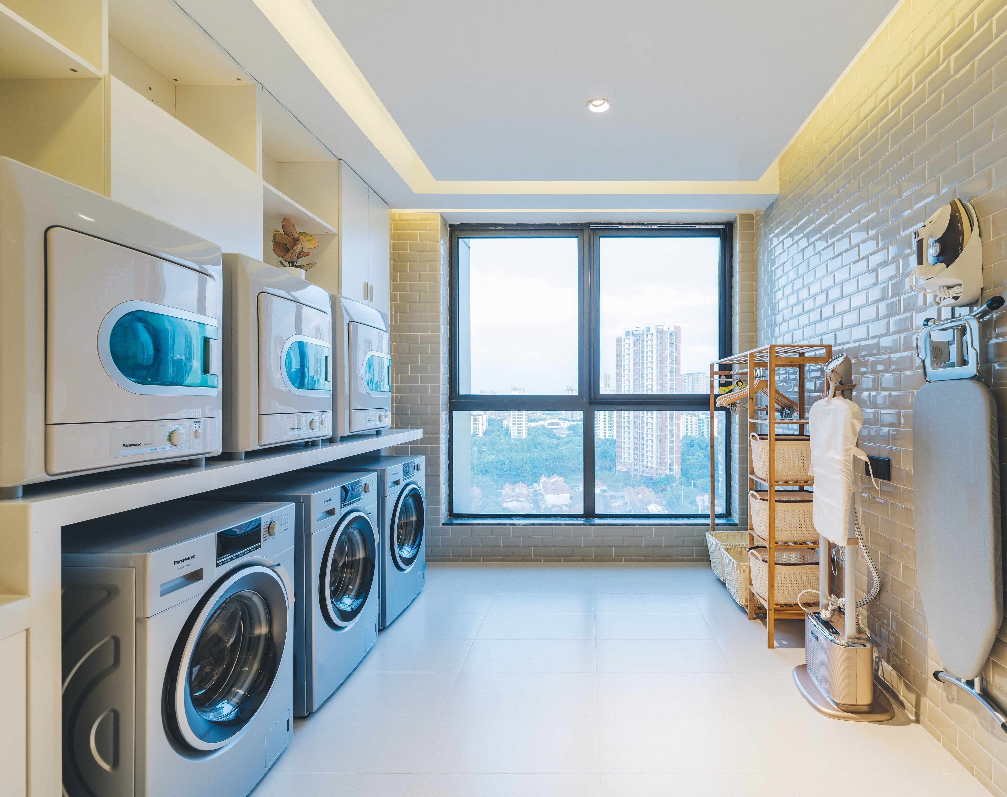 A modern laundry room with stacked washing machines, a drying rack, and a large window offering a city view.