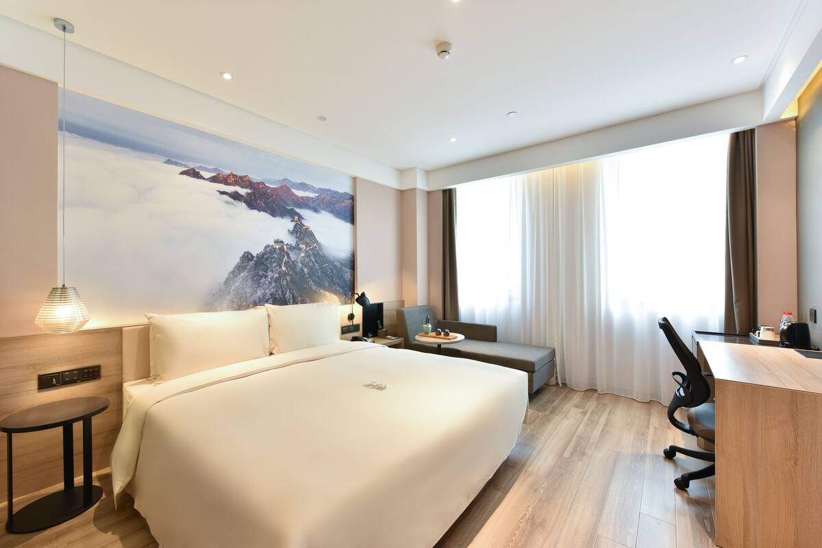 Une chambre d’hôtel moderne, dotée d’un grand lit, d’un bureau, d’une chaise et offrant une vue sur les montagnes par la fenêtre.