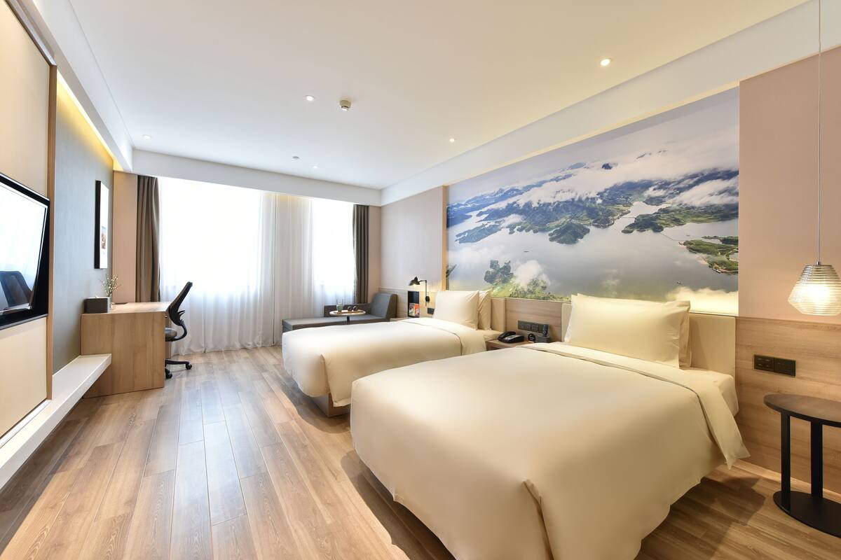 Une chambre d’hôtel avec deux lits, un bureau, une chaise, une télévision et une grande fenêtre avec des rideaux.