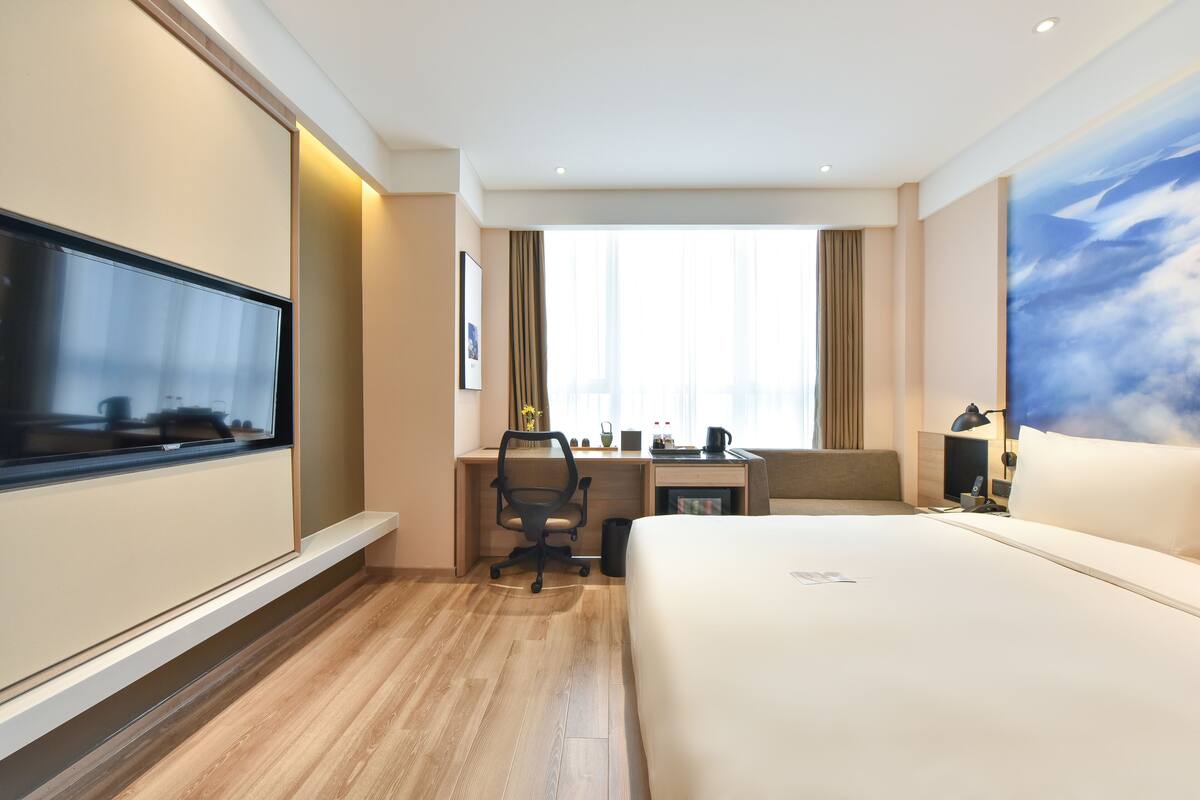 Une chambre d’hôtel avec un lit, un bureau et une chaise, une télévision et une grande fenêtre avec des rideaux.
