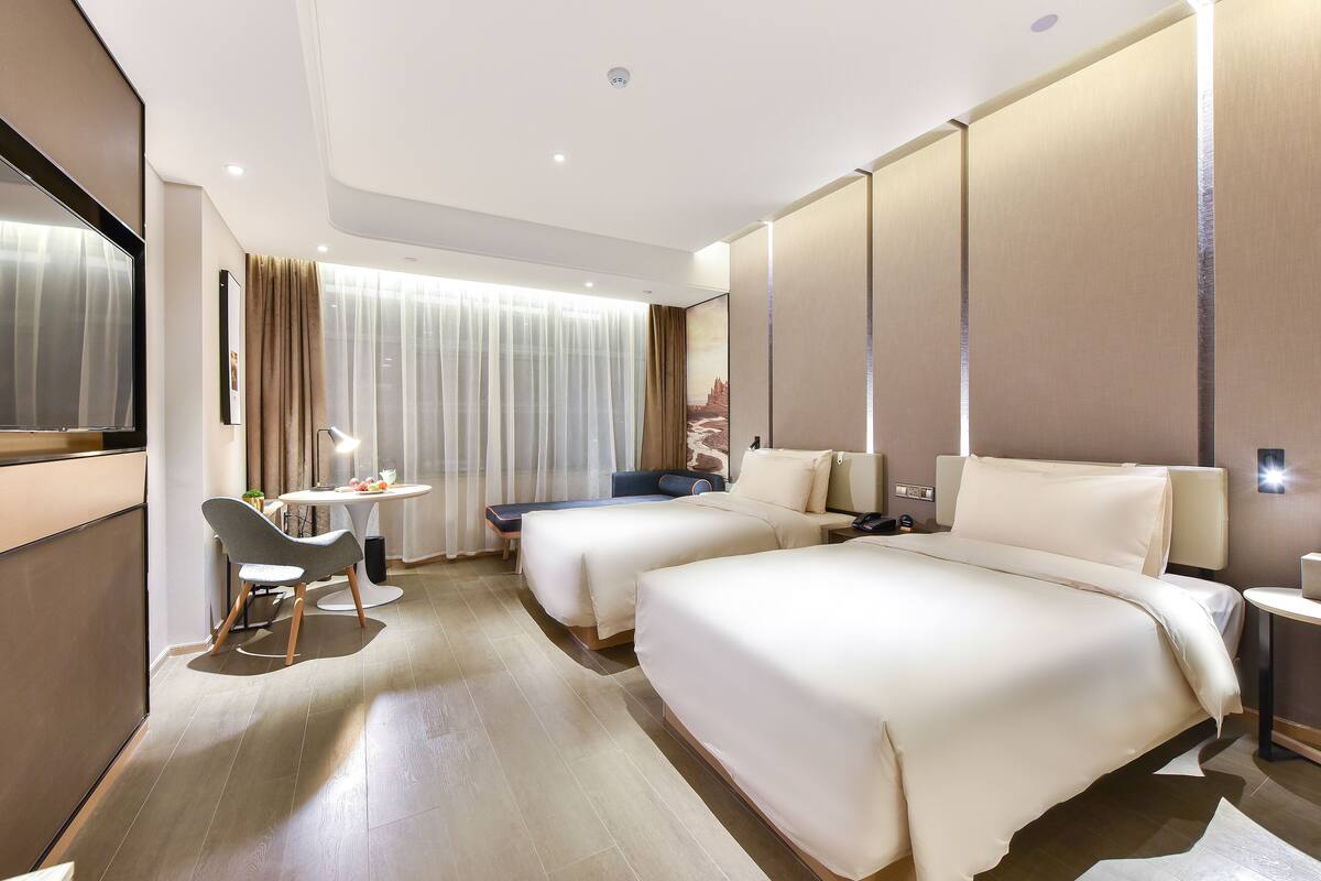 A hotel room with two beds, a desk, a chair, and a small table.
