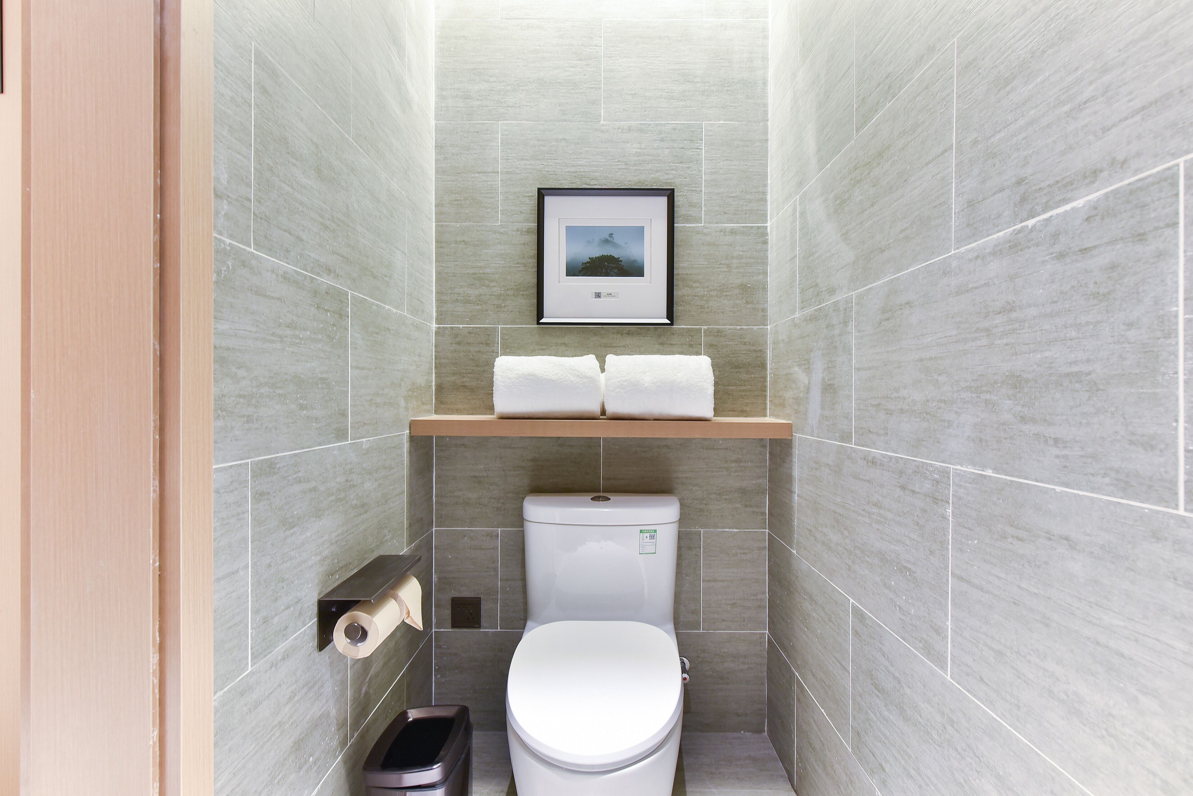 A compact bathroom with a toilet, a towel rack, and a framed picture on the wall.