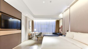 Una habitación de hotel moderna con una cama grande, un escritorio con una silla, un televisor de pantalla plana y un ventanal con cortinas translúcidas.