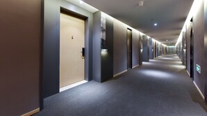Un largo y estrecho pasillo de hotel con varias puertas, algunas con manijas visibles y otras con acceso por tarjeta.
