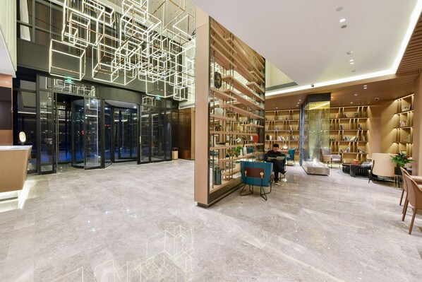 A modern lobby with a marble floor, a geometric light installation, a bookshelf, and seating areas.
