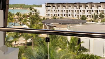 Een balkon met uitzicht op een resort, inclusief een zwembad, palmbomen en een gebouw met meerdere balkons.
