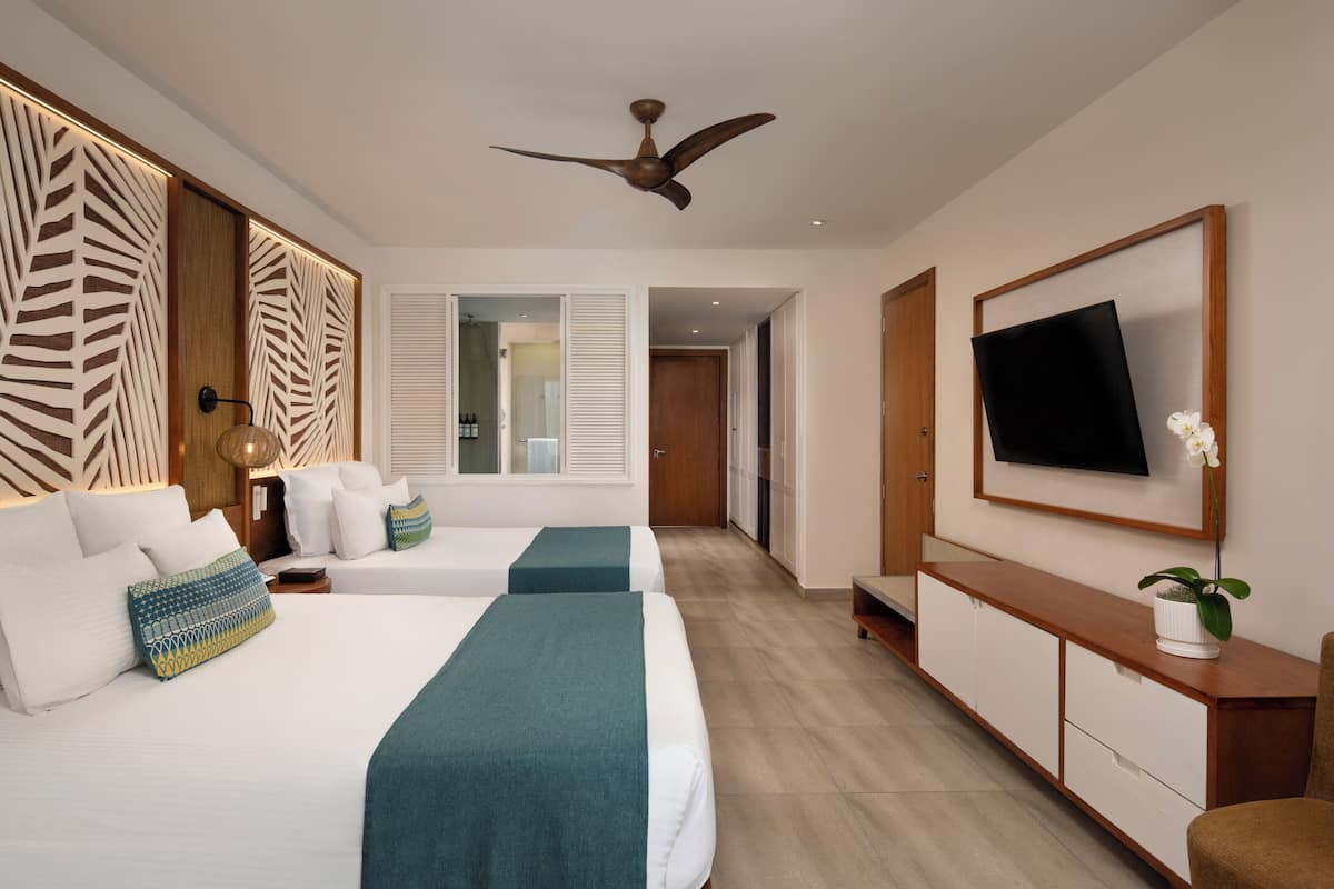 A hotel room with two beds, a TV, a ceiling fan, and a wooden cabinet.