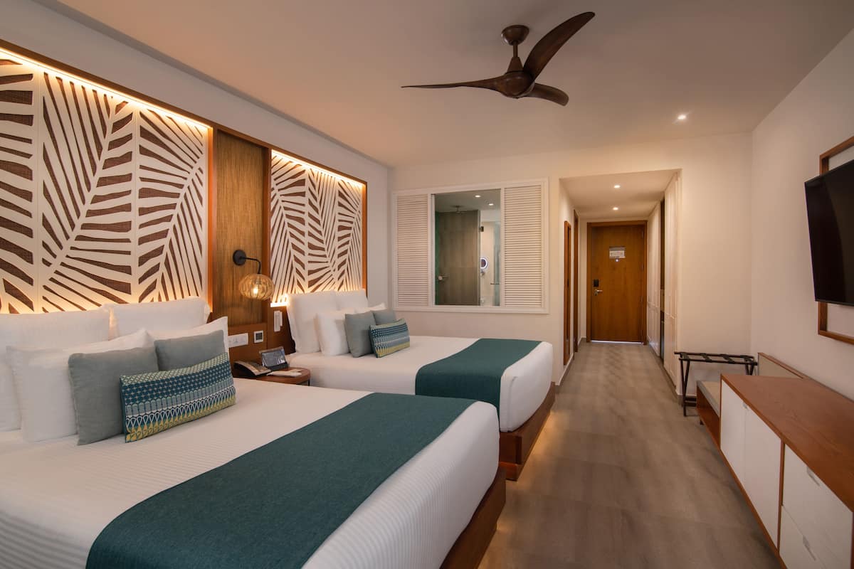 A hotel room with two beds, a ceiling fan, a TV, and a wooden desk.