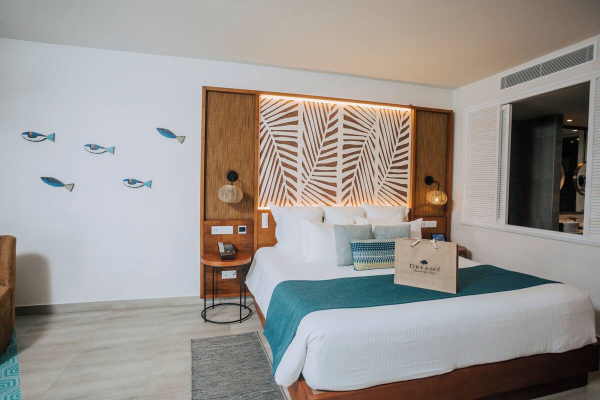 A modern bedroom with a wooden headboard, a bed with white bedding, a teal throw blanket, and a small side table with a lamp.