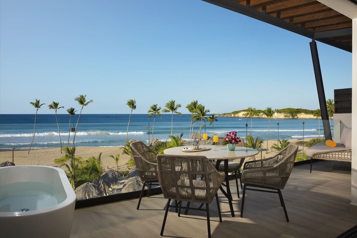 A balcony with a view of the ocean, wicker furniture, and a table with a vase of flowers.