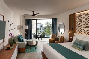 A modern hotel room with a bed, a desk, a chair, a small table, and a balcony with a view of the outside. - Dreams Macao Beach Punta Cana - All Inclusive (Punta Cana)