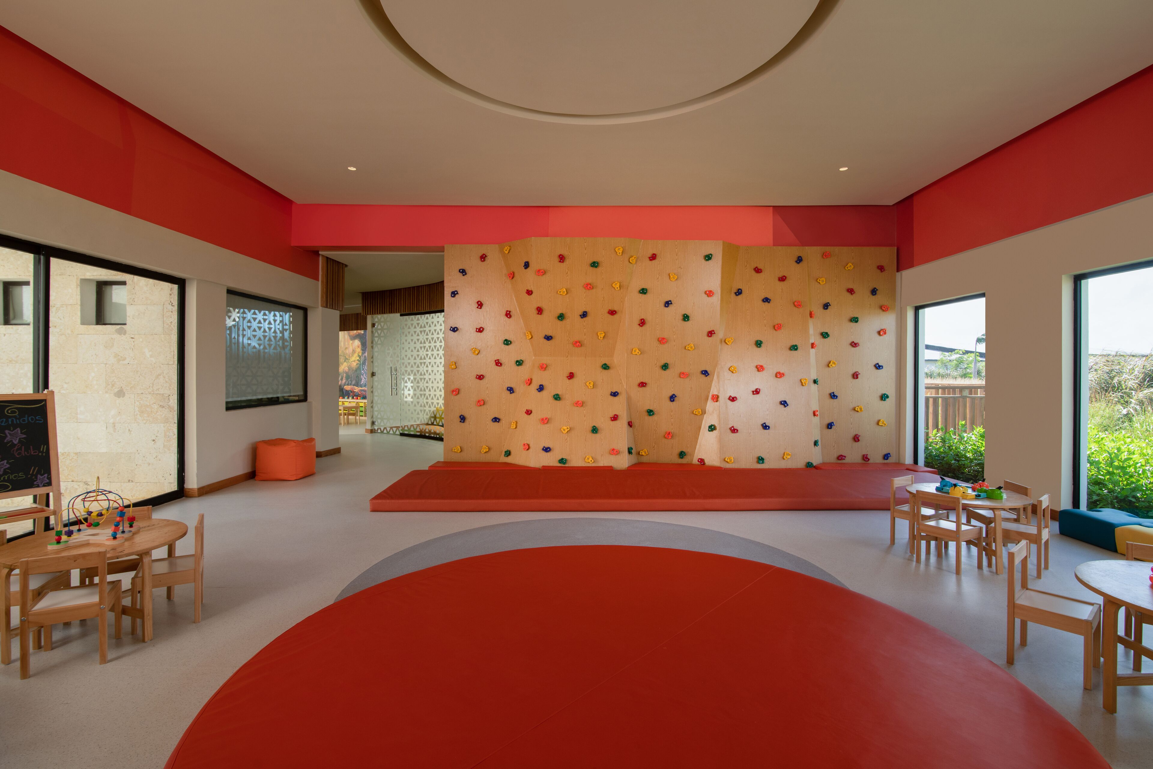 A modern children's play area with climbing walls, seating, and tables.