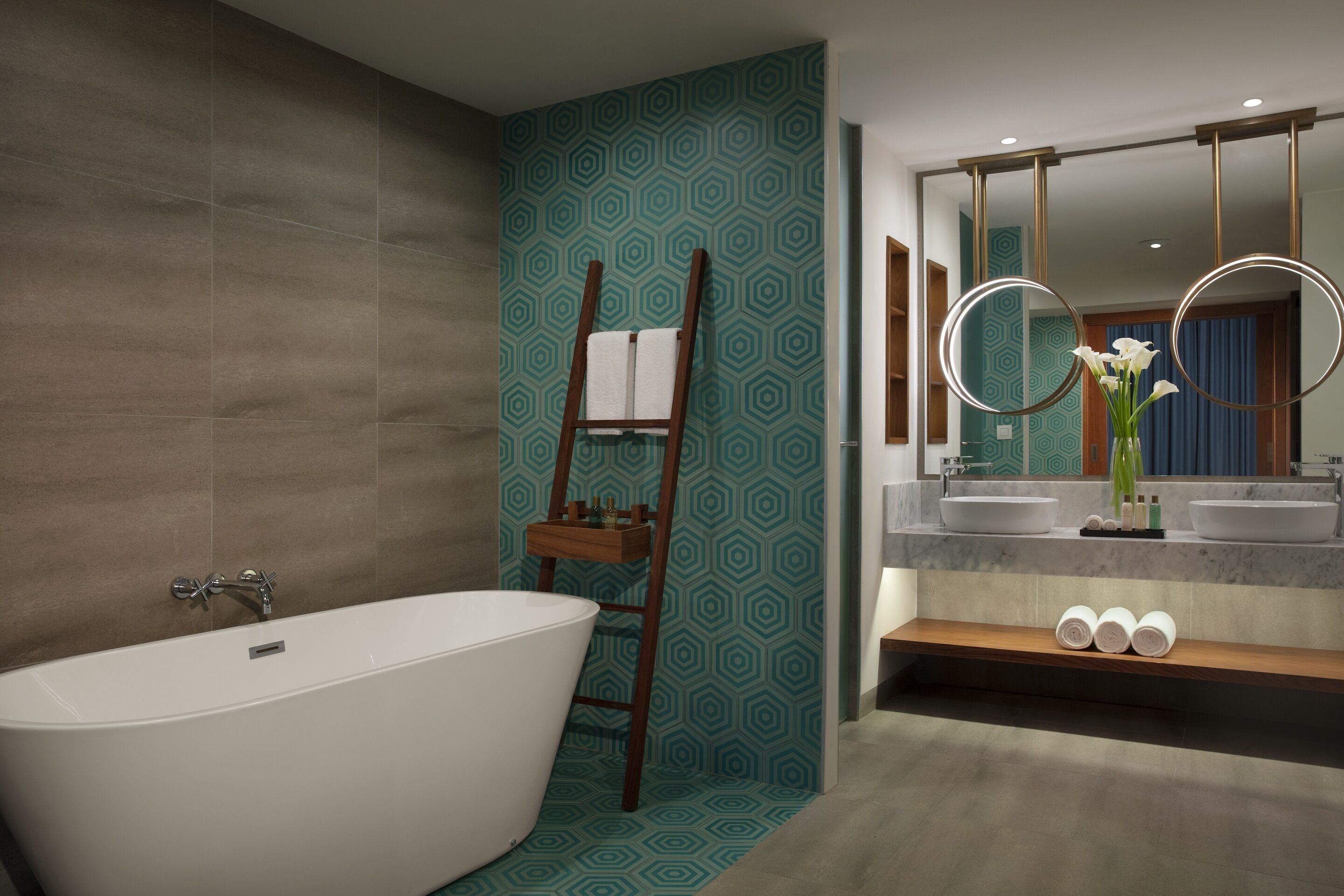 Une salle de bain moderne avec une baignoire sur pieds, une échelle en bois, un meuble-lavabo avec deux vasques et un miroir doté de lumières circulaires.
