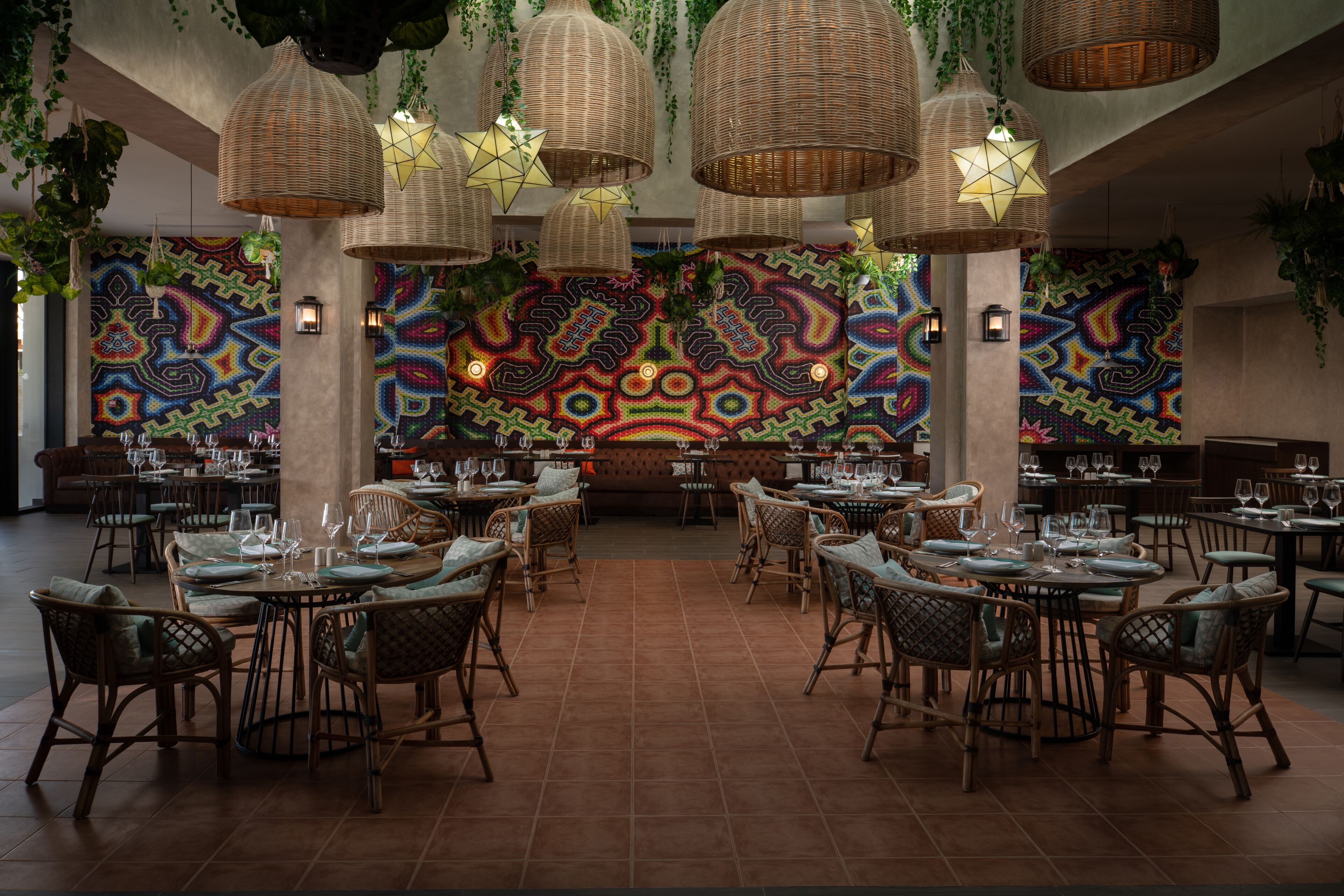 Um restaurante com mobiliário de vime, luminárias pendentes e obras de arte coloridas nas paredes.