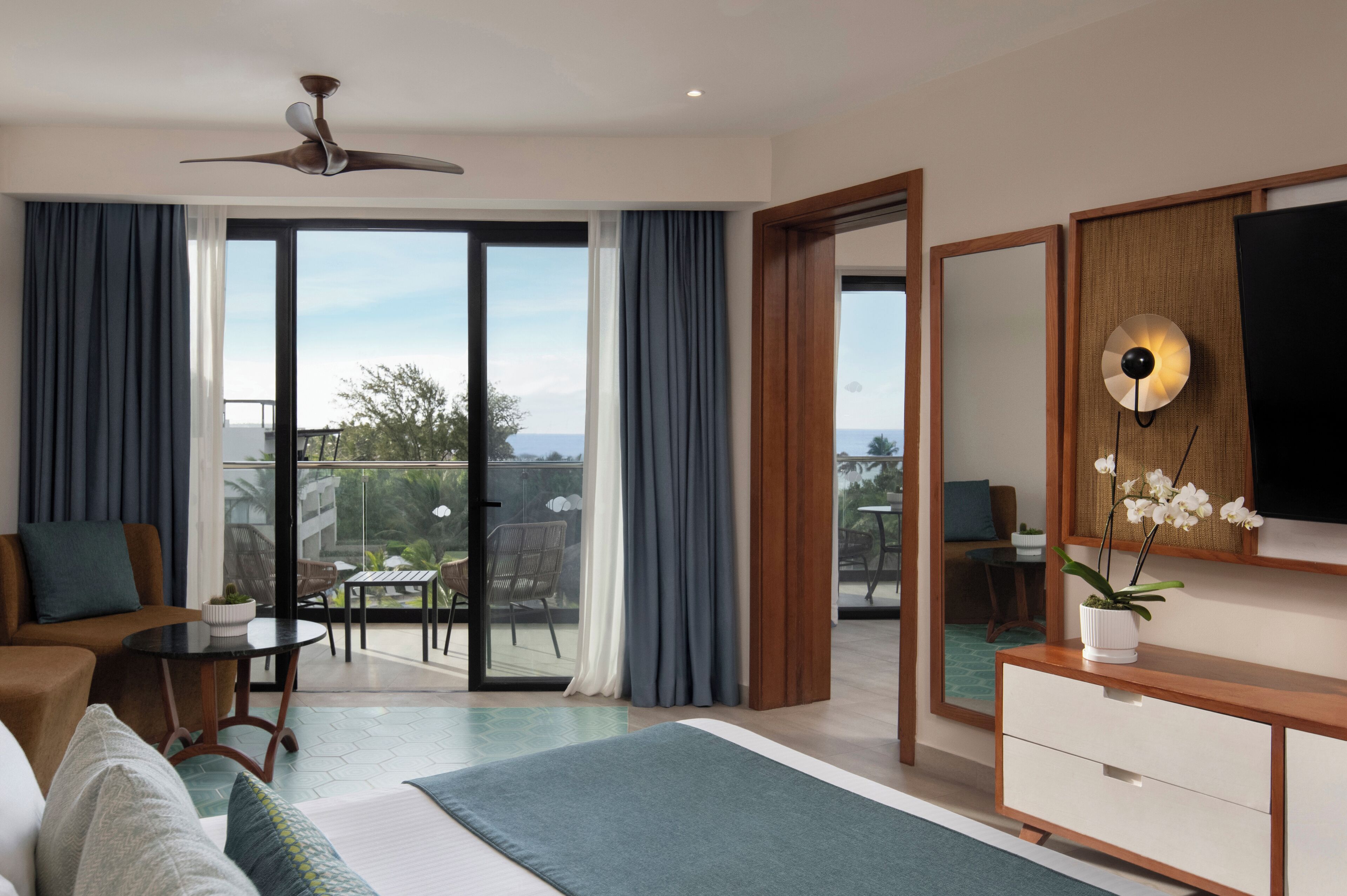 Et moderne hotelværelse med balkon, loftventilator, fladskærms-TV og en trækommode.