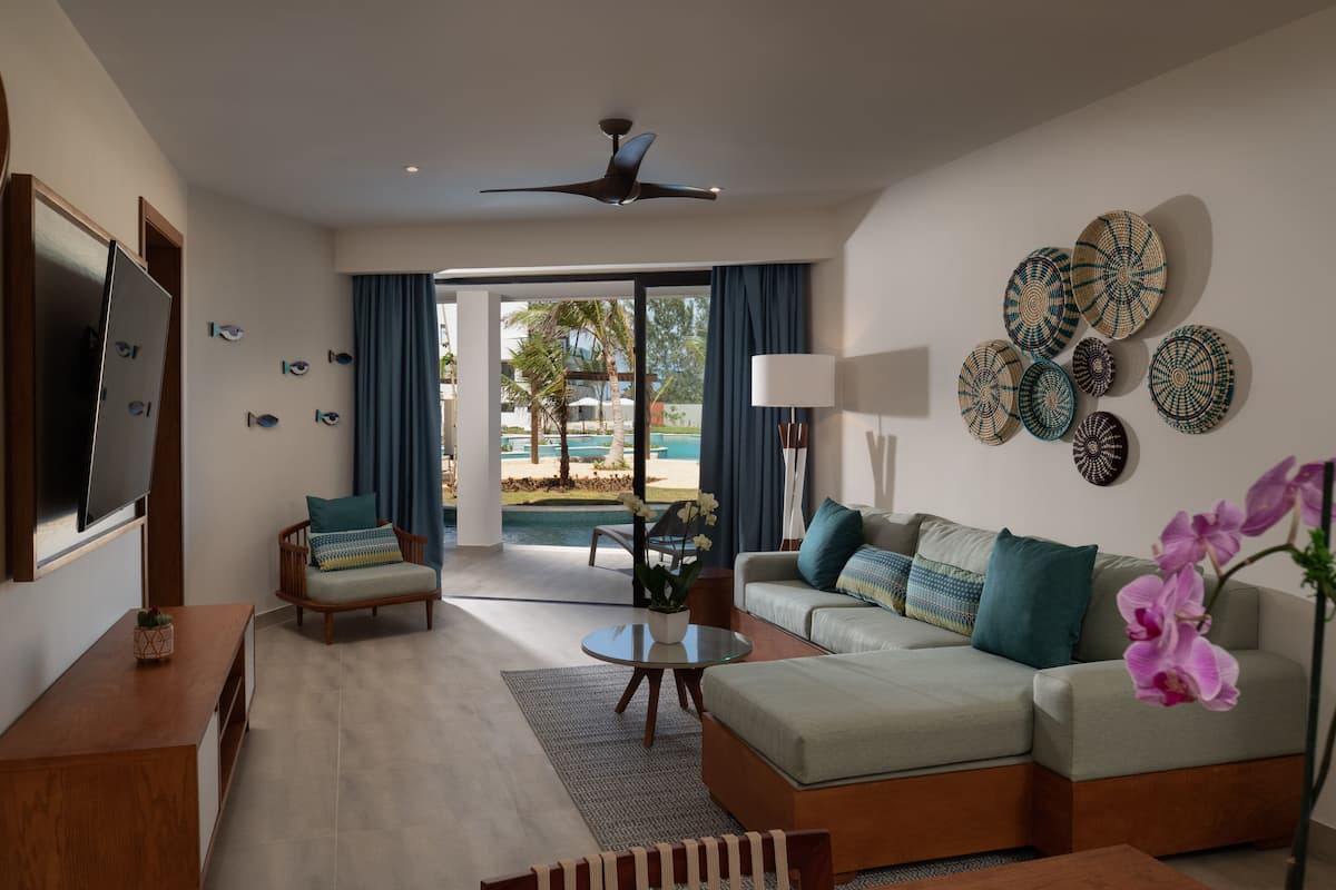 A modern living room with a sofa, armchairs, a coffee table, and a TV. There are decorative plates on the wall and a ceiling fan.