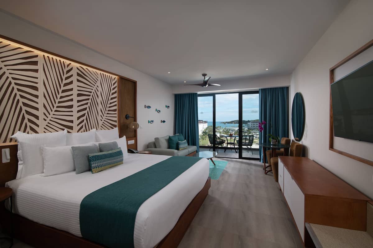 A modern hotel room with a large bed, a desk, a balcony with a view, and a ceiling fan.