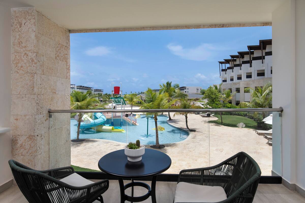 A balcony with a view of a pool area, including a water slide and palm trees.
