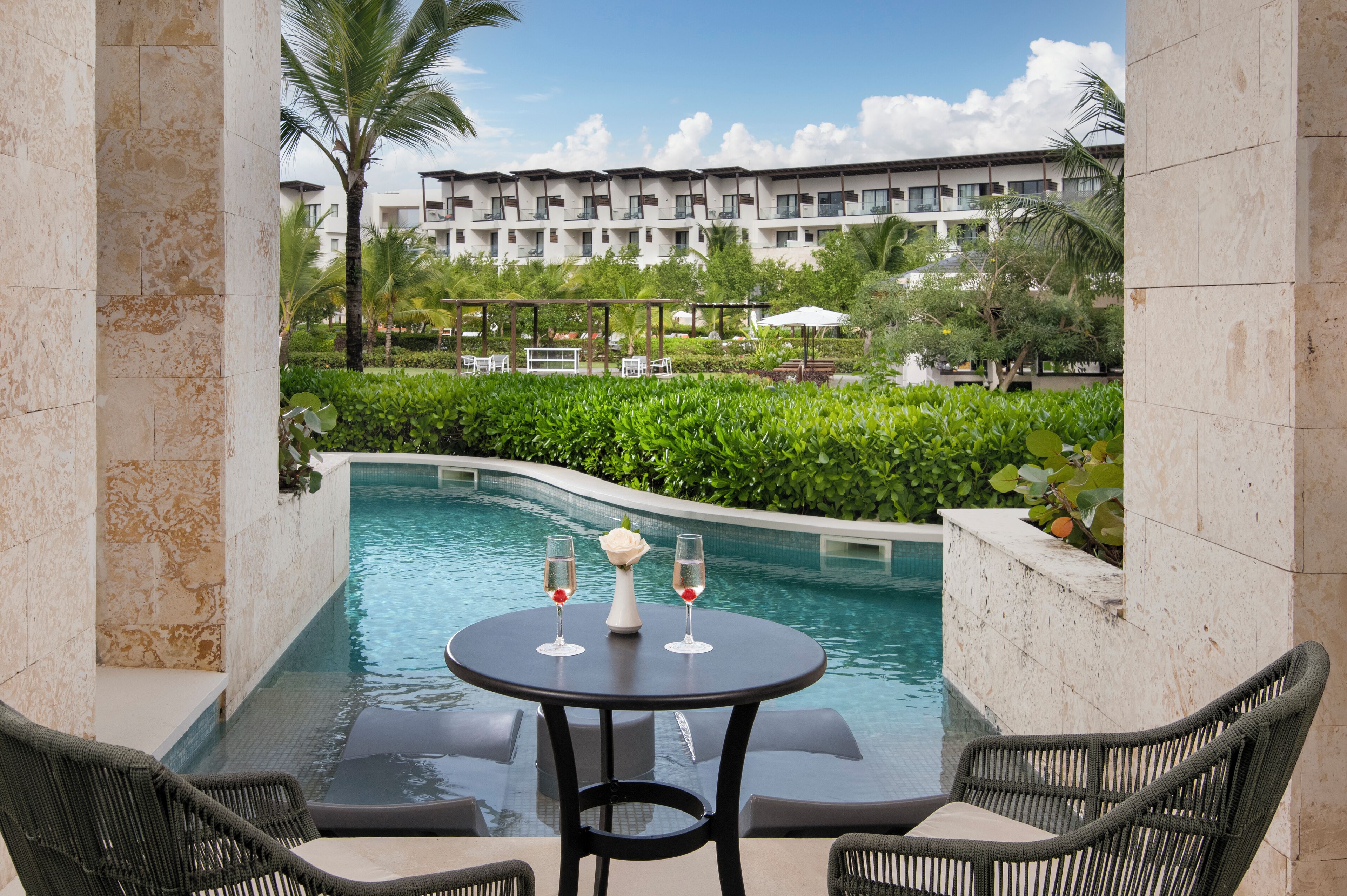 Un espace aménagé au bord de la piscine, avec une table et deux chaises, une piscine, et un bâtiment avec des balcons en arrière-plan.