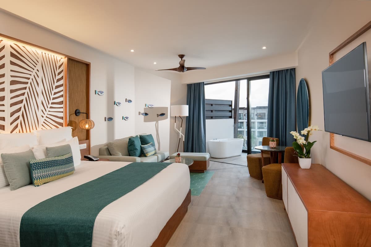 A modern hotel room with a large bed, a sofa, a desk, and a balcony with a view.