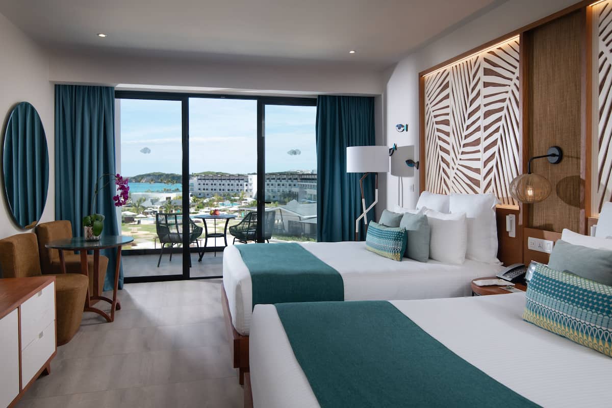 A hotel room with two beds, a desk, and a view of the ocean.