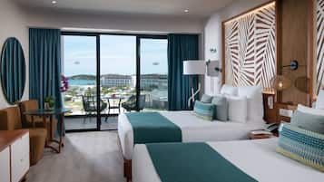 A hotel room with two beds, a desk, and a view of the ocean.