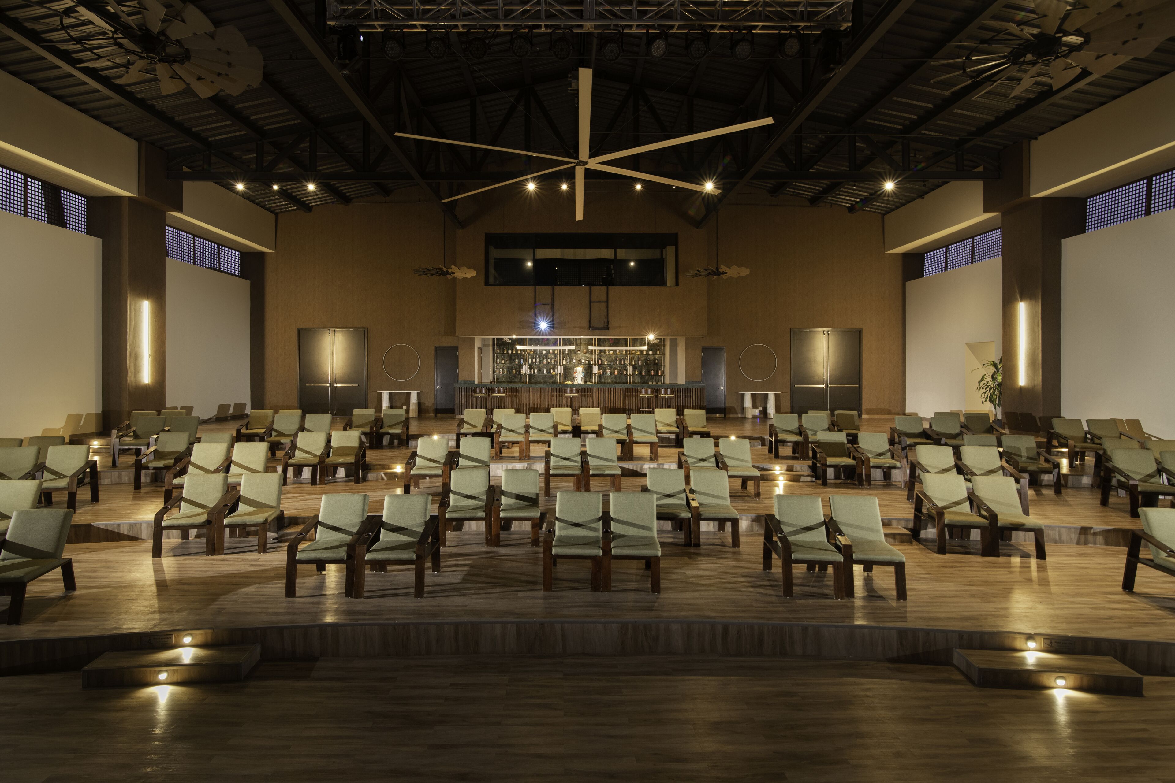 A spacious hall with rows of chairs facing a stage, equipped with a ceiling light fixture and a large window.