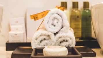 A neatly arranged set of toiletries including a rolled towel, a soap bar, and bottles of lotion.