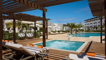 A poolside area with lounge chairs, umbrellas, and a wooden pergola.