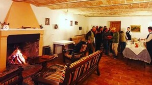 Un interior rústico con techo de piedra, una chimenea, muebles de madera y un grupo de personas reunidas alrededor de una mesa.