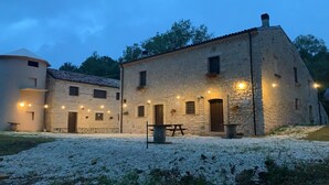 Un edificio de piedra con varias ventanas y puertas, un patio de grava e iluminación exterior.