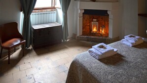 Un cuarto acogedor con chimenea, una silla de madera, una cama con toallas ordenadas y una ventana con cortinas.
