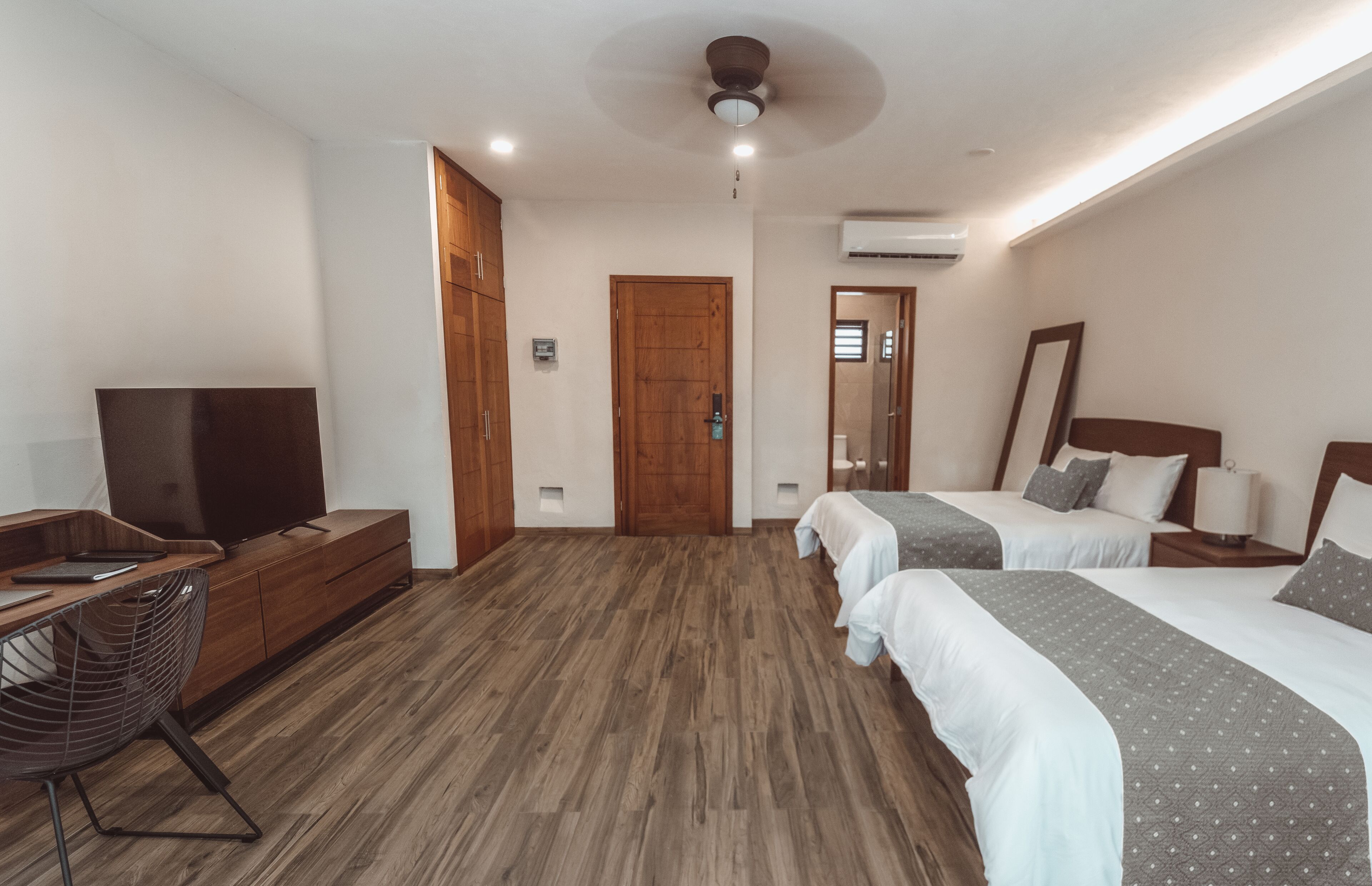 Habitación de hotel con dos camas, un escritorio con silla, televisor y ventilador de techo.