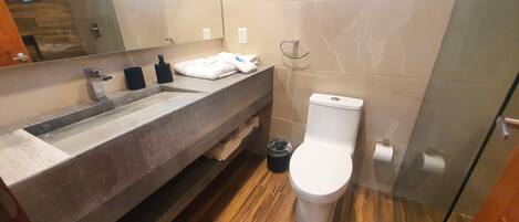 A modern bathroom with a large mirror, a sink, a toilet, and a trash bin.