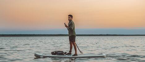 A person standing on a paddleboard in a body of water with a sunset in the background.
